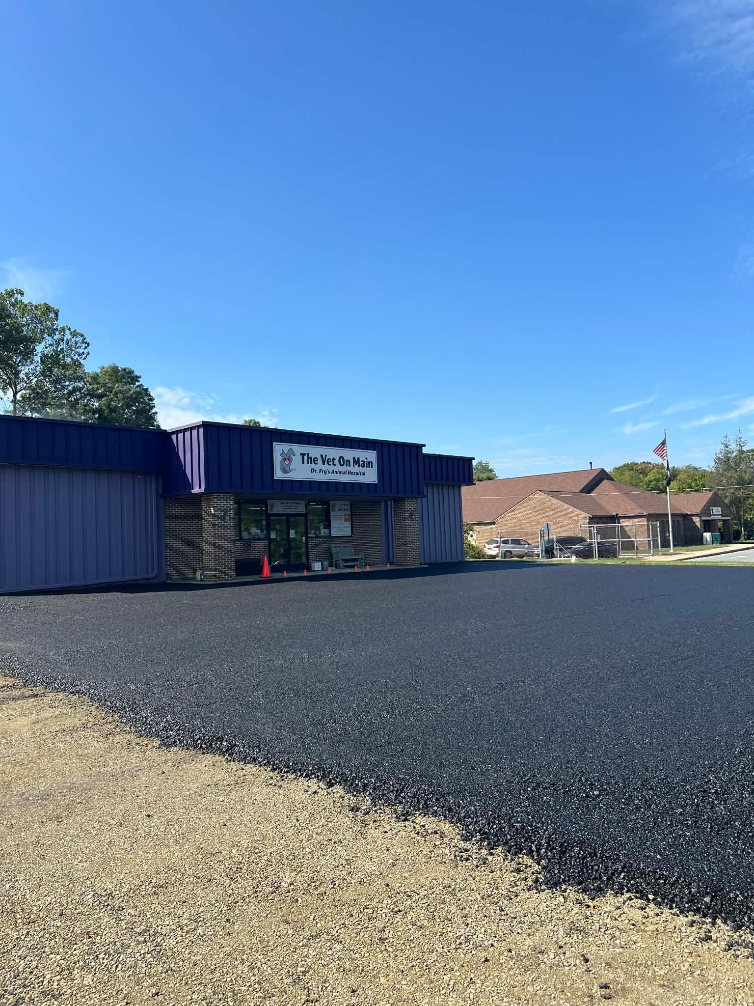A storefront with a purple facade and a sign, featuring a newly paved asphalt parking lot under a clear blue sky.