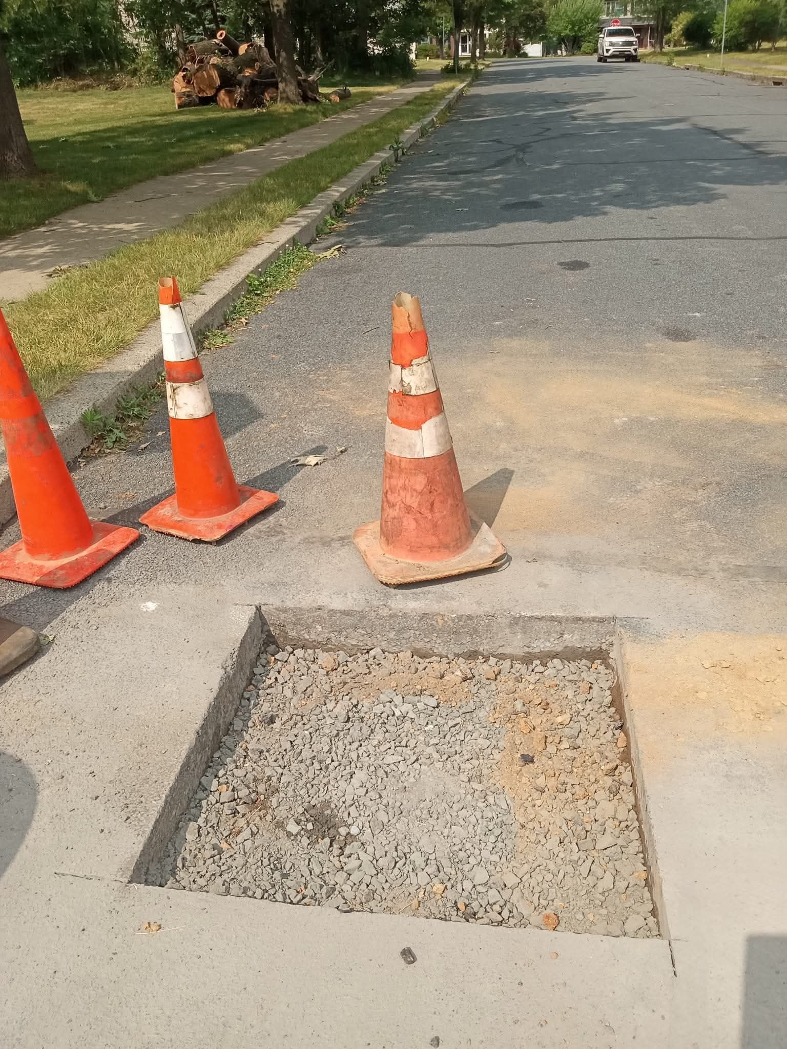 Street repair area with orange traffic cones and a square section of pavement removed.