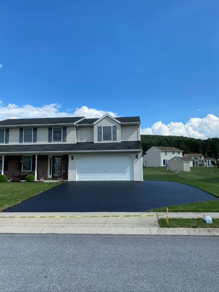 Two-story house with a newly paved, black driveway on a sunny day.