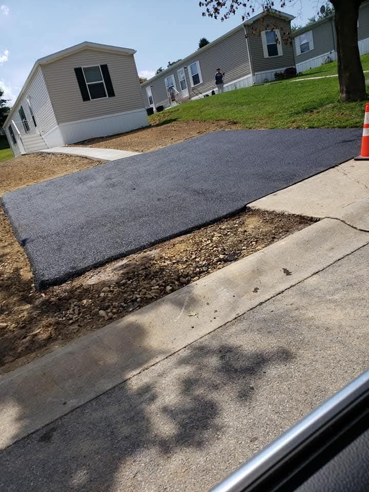 New asphalt driveway next to a curb and mobile homes.  A bright orange cone sits on the edge.