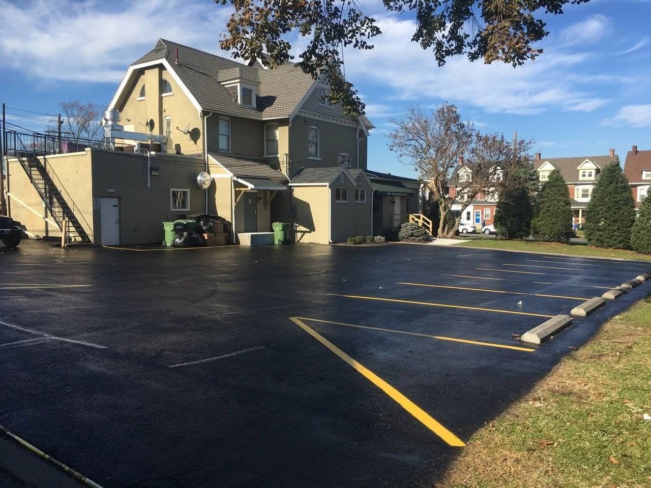 Asphalt parking lot next to a light-colored building with a few parked cars in the distance.