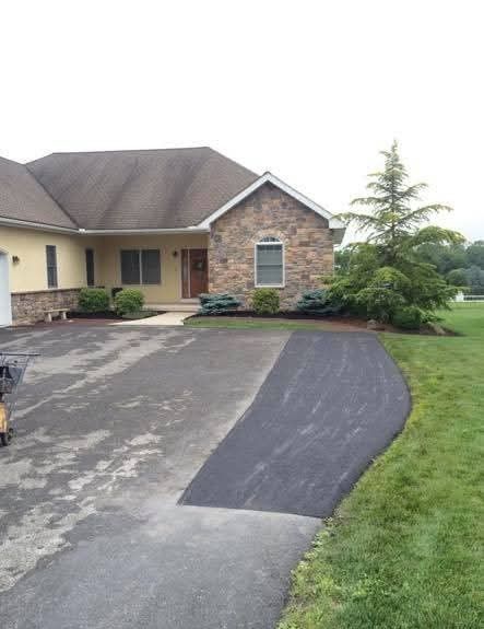 Partially paved driveway in front of a house with stone facade and landscaping.