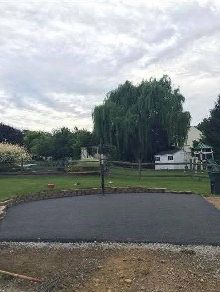 Newly paved dark asphalt area with a weeping willow tree and a cloudy sky in the background.