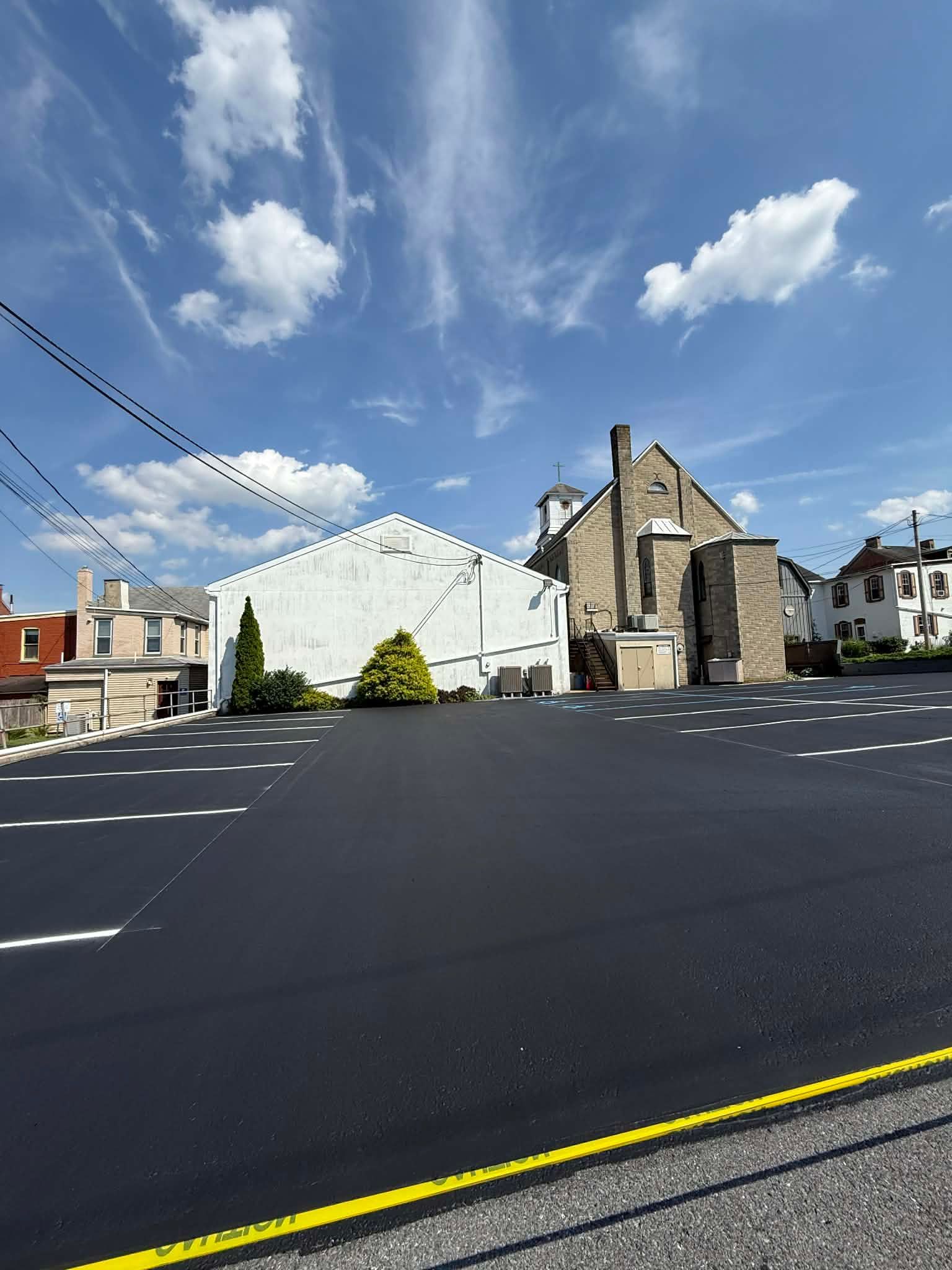 Exterior shot of a church with a black asphalt parking lot, blue sky, and white clouds.
