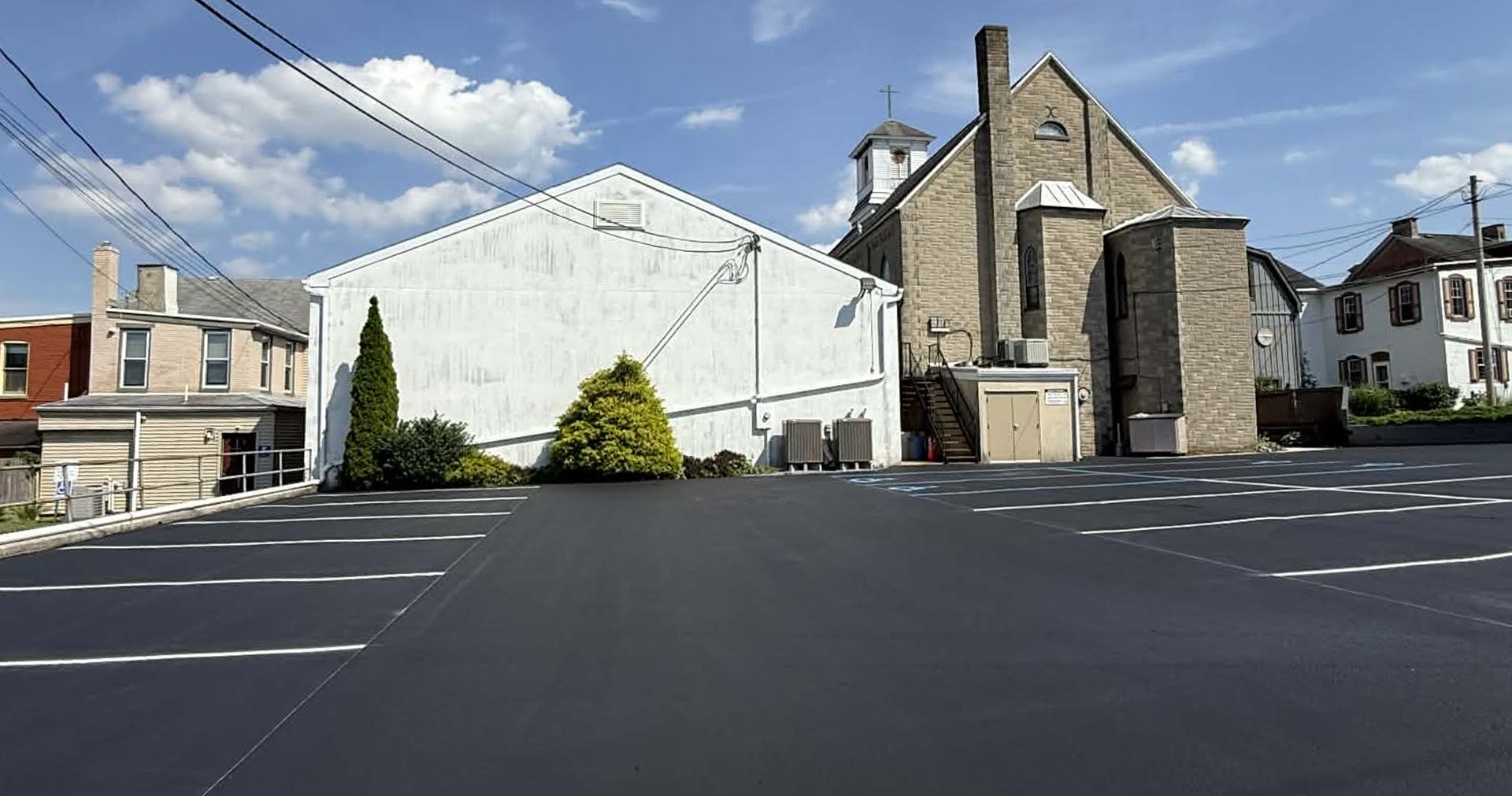 A parking lot in front of a white warehouse and an adjacent historic stone building under a blue sky.