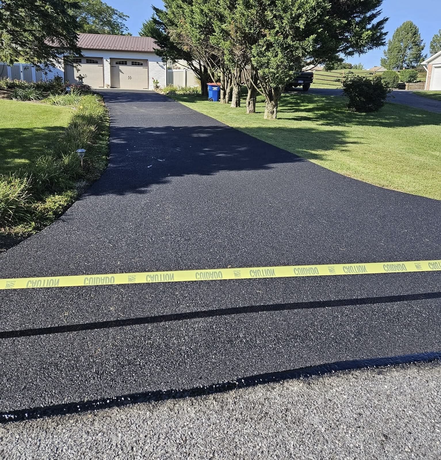 A freshly paved, dark asphalt driveway leading to a garage, blocked by yellow caution tape.