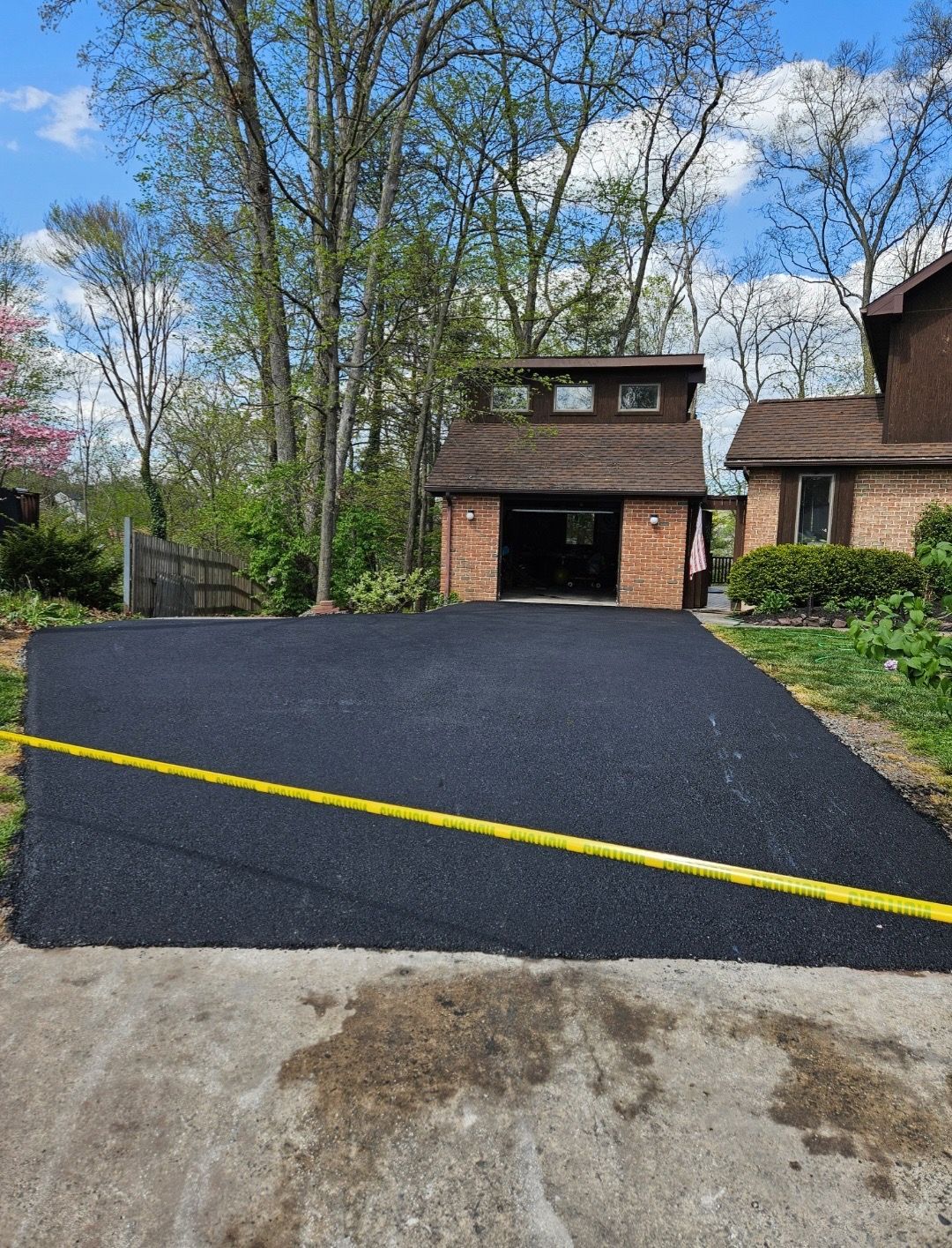 A freshly paved black asphalt driveway leading to a garage next to a house, with a yellow tape line across the foreground.