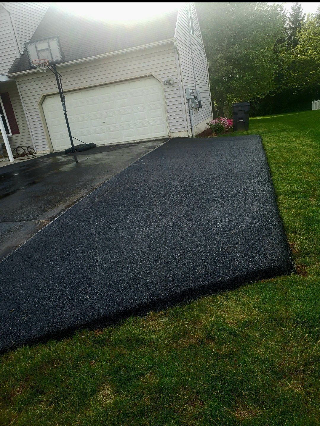 Driveway paved with fresh black asphalt, beside a green lawn and a house.