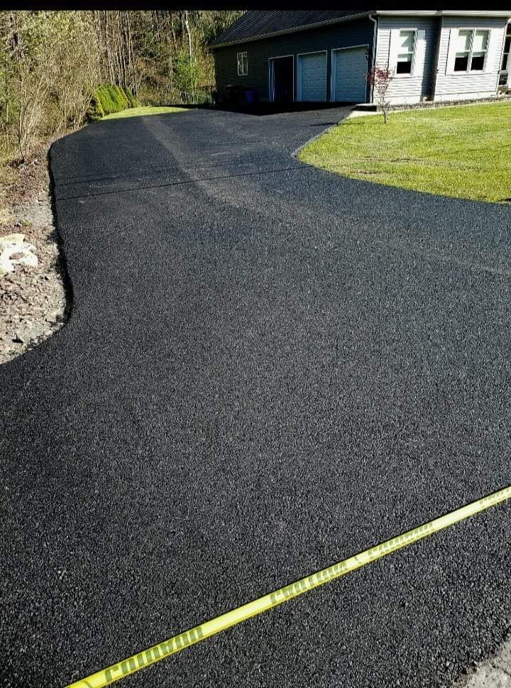 Newly paved asphalt driveway leading to a house with a green lawn. Yellow caution tape.