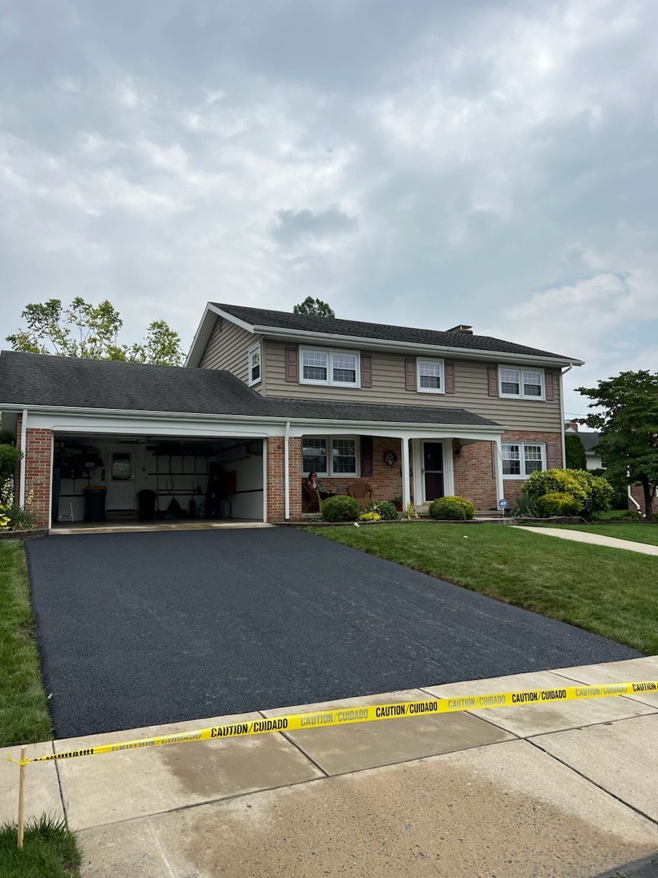 Two-story house with newly paved black driveway and attached garage, under an overcast sky.