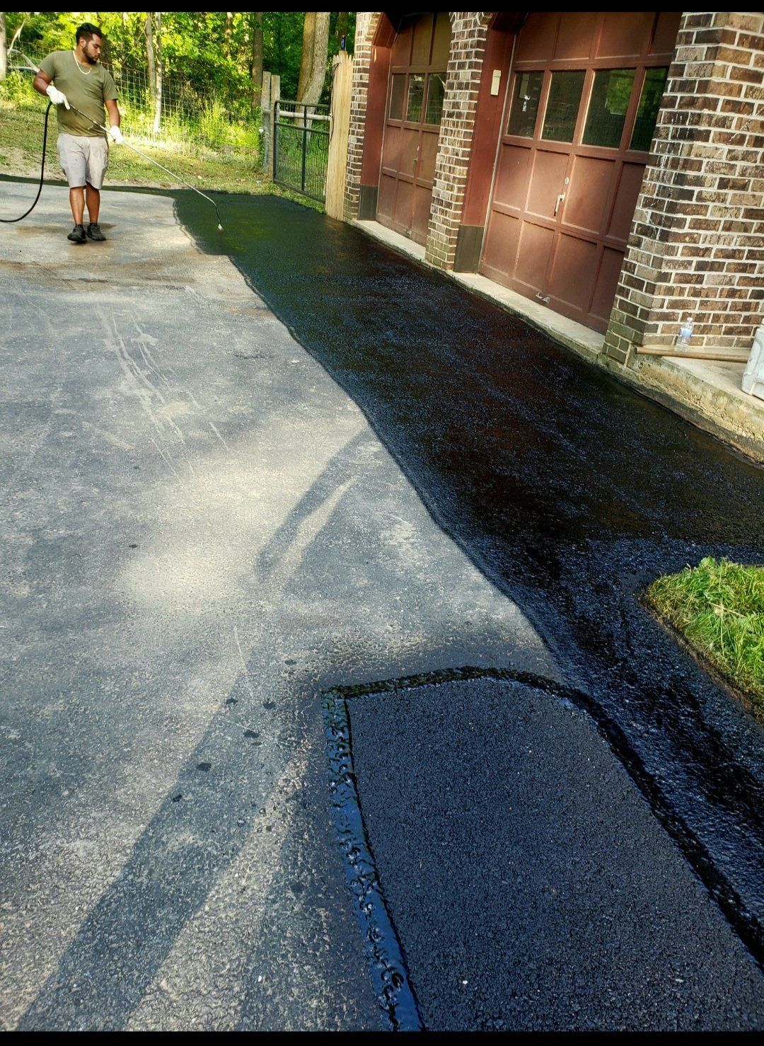 Man spraying newly paved asphalt driveway next to a brick building.