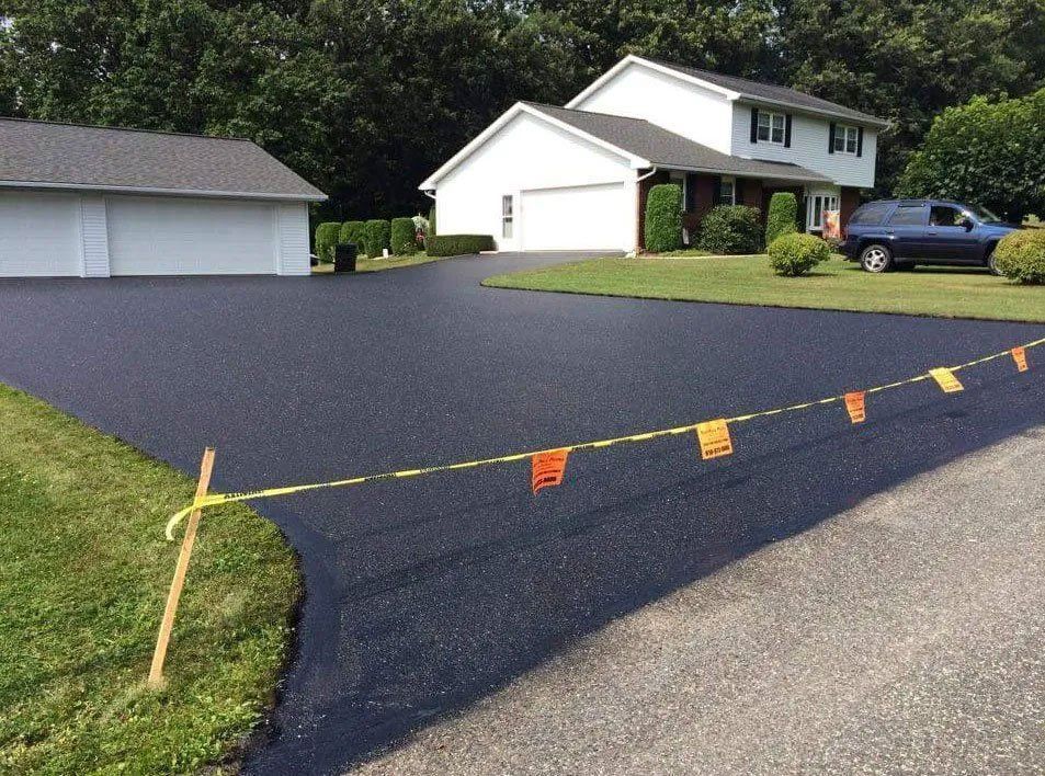 Newly paved black asphalt driveway in front of a white house with a detached garage.