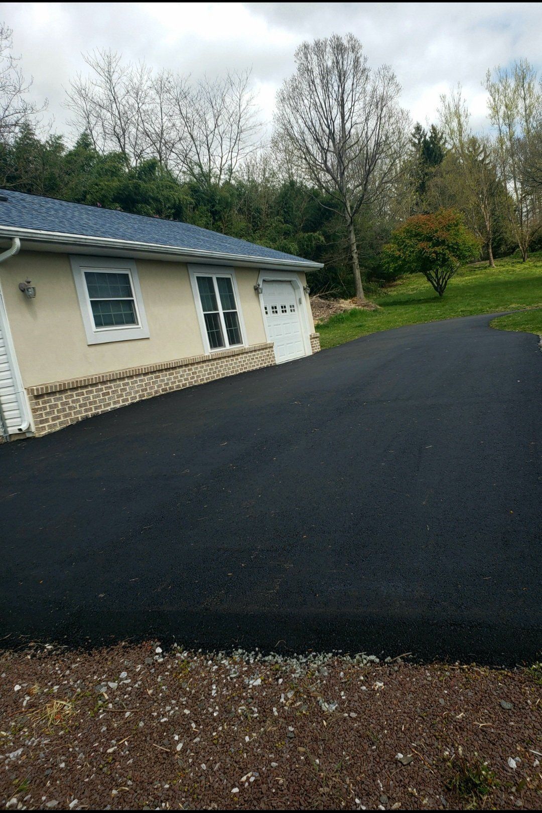 A cream-colored house with a blue roof, stone accents, and a freshly paved black asphalt driveway.