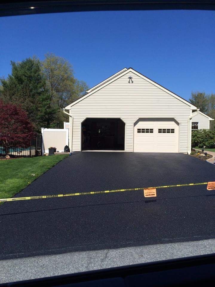 A newly paved black asphalt driveway leads to a white two-car garage with one open bay under a clear blue sky.