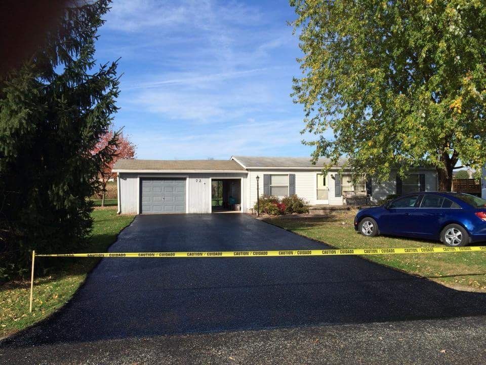 A single-story residential house with a newly paved asphalt driveway cordoned off by yellow caution tape.