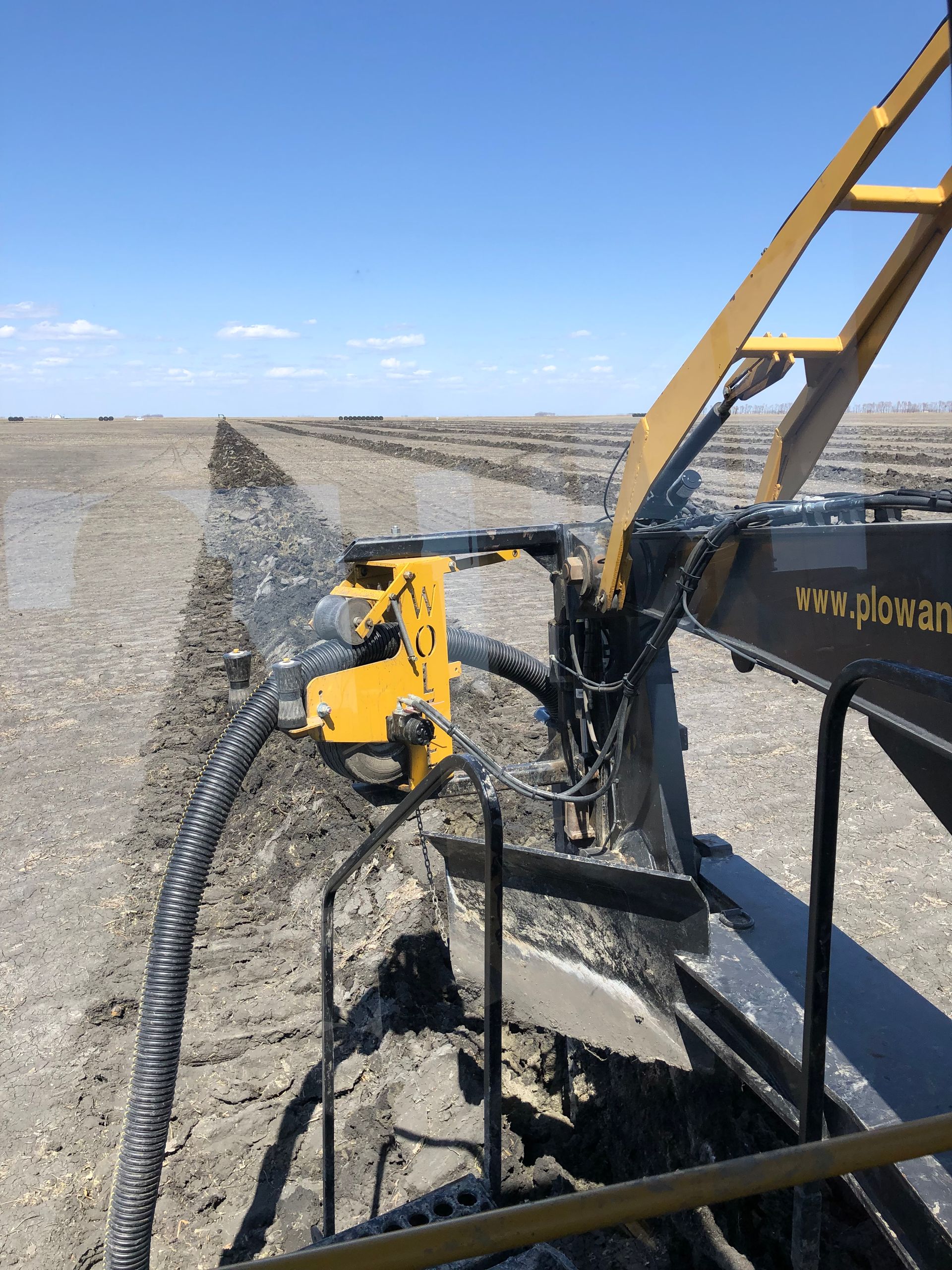 A yellow and black tractor is plowing a field with a hose attached to it.