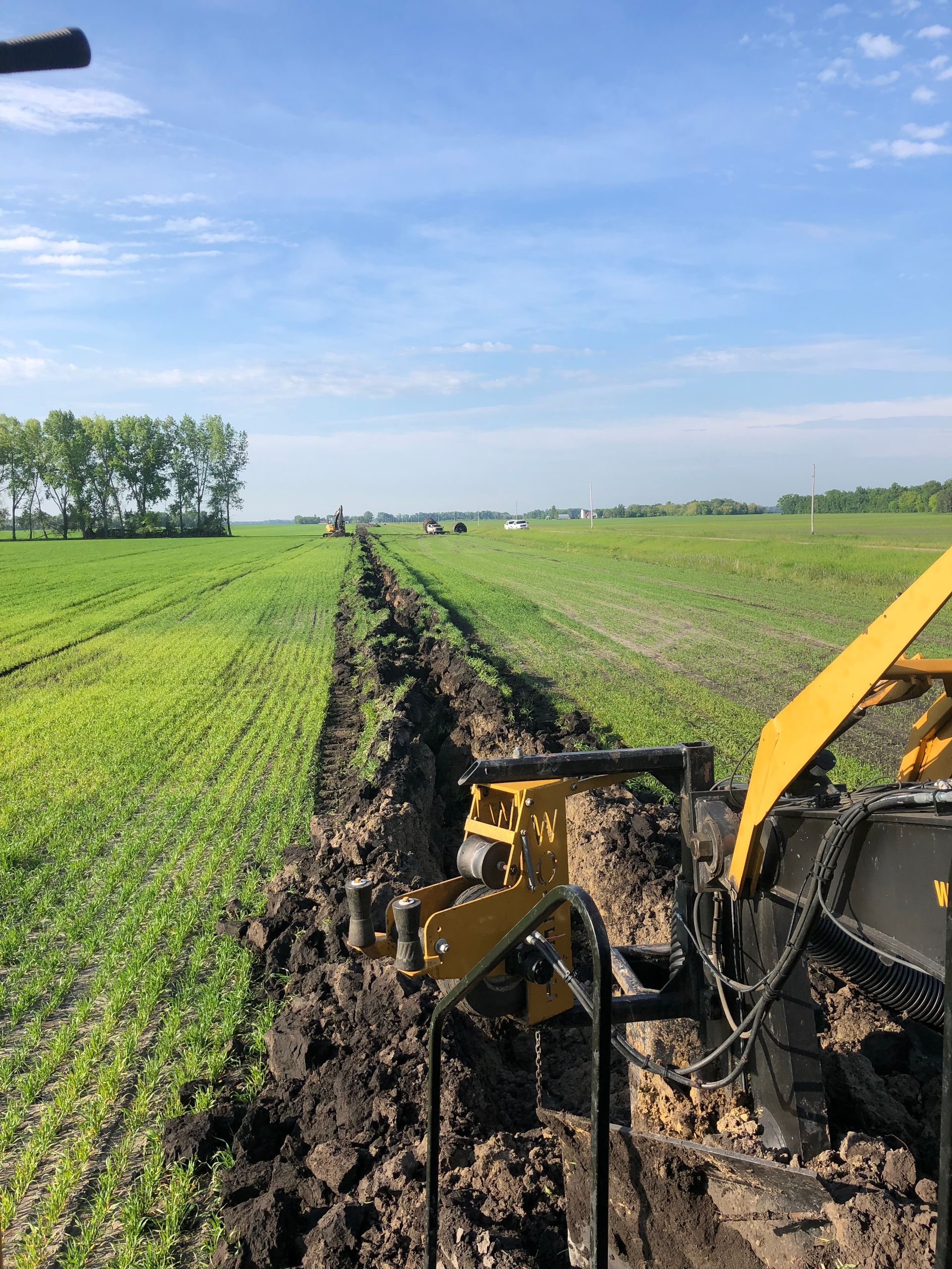 A yellow tractor is plowing a field of grass.