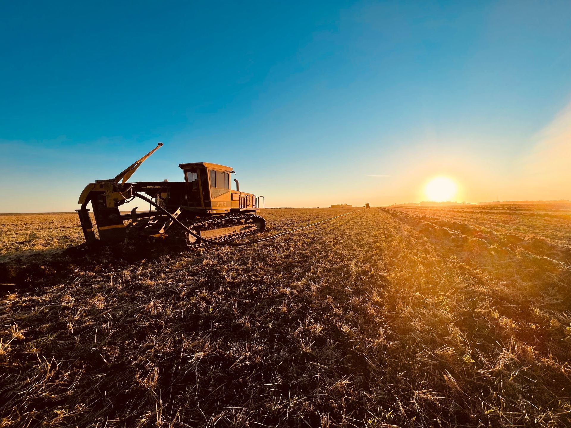 A bulldozer is plowing a field at sunset.
