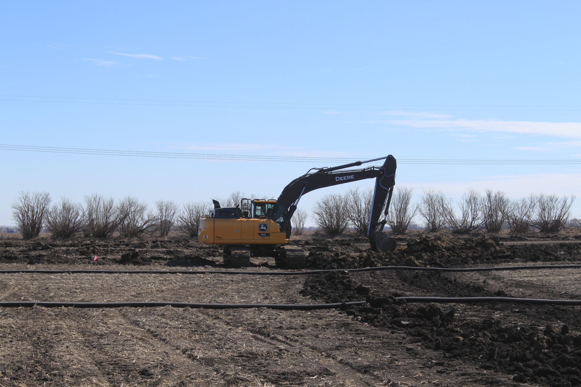 A large yellow excavator is working on a dirt field