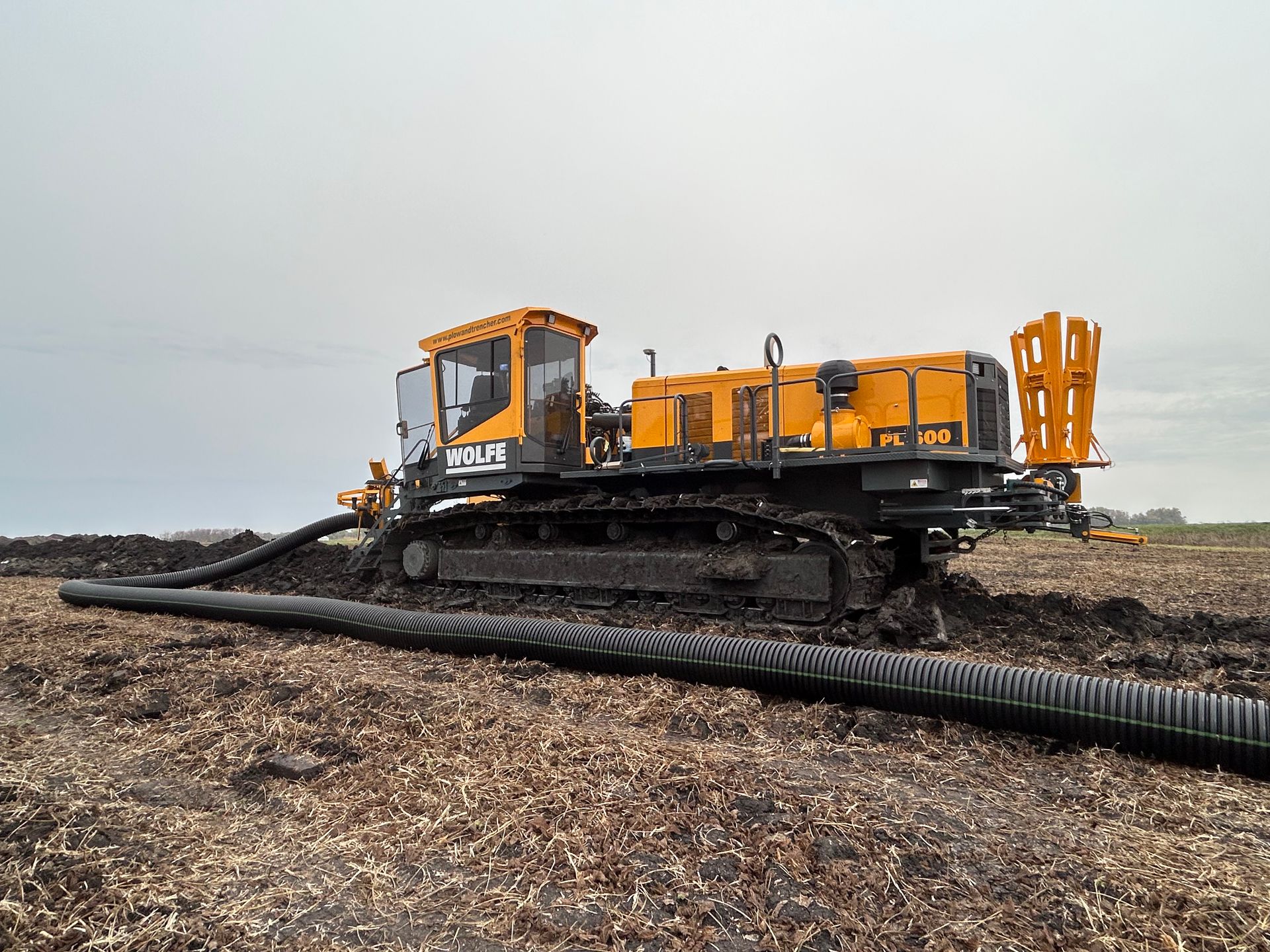 A yellow and black construction vehicle is driving through a dirt field.