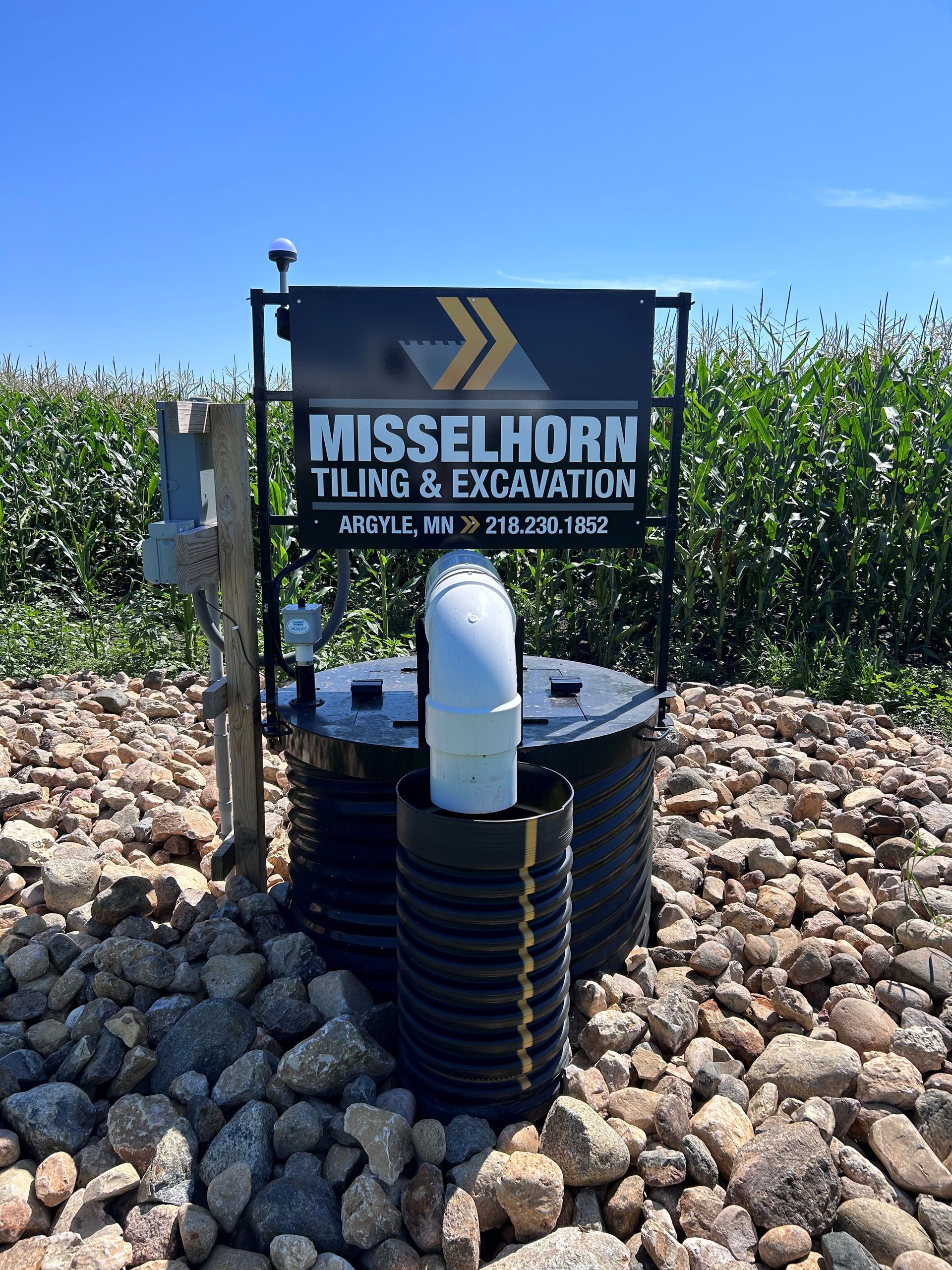 A sign for misselhorn tiling and excavation is sitting on top of a pile of rocks.