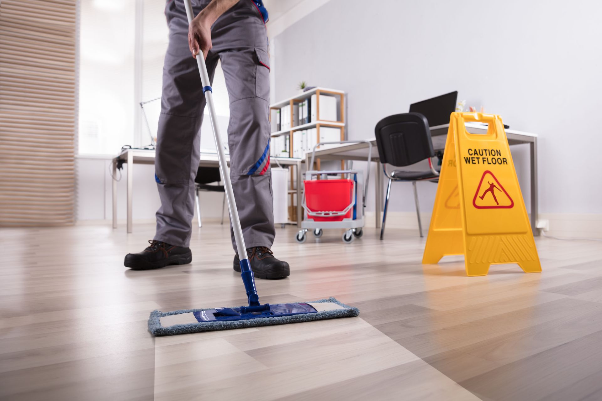 A man is mopping the floor in an office next to a caution sign.