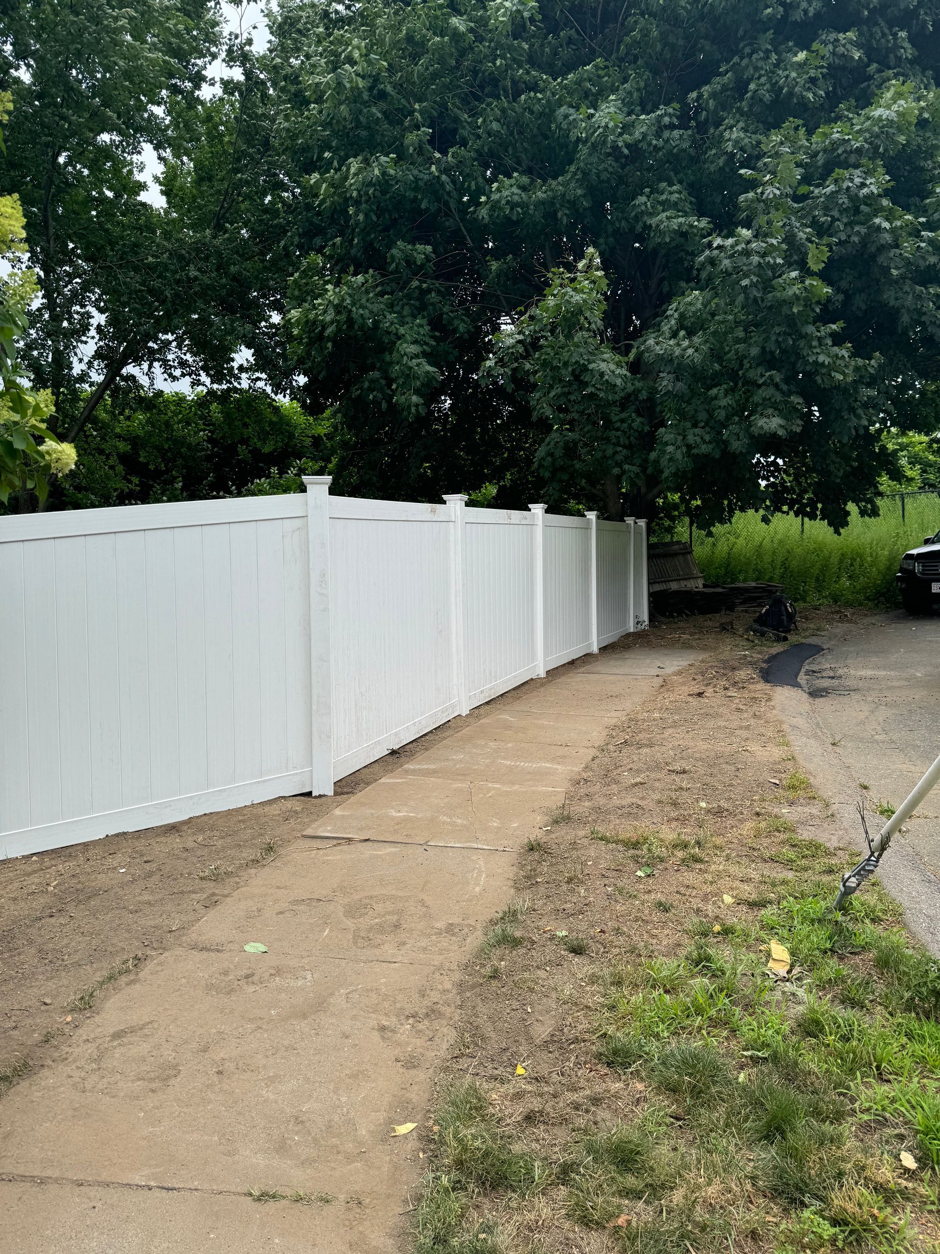 White vinyl fence along a dirt path, trees in background.