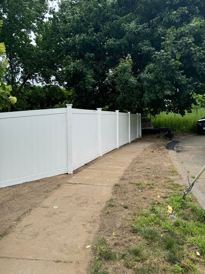 White vinyl fence along a dirt path, trees in background.