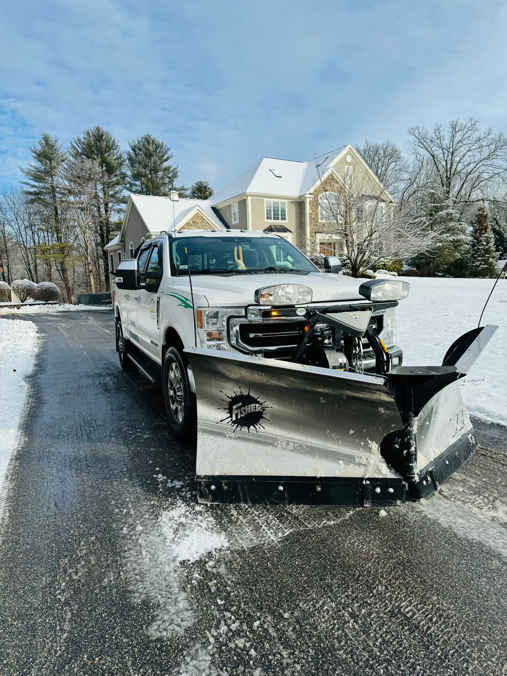 Person using a snow blower to clear a driveway in front of a snow-covered suburban house.