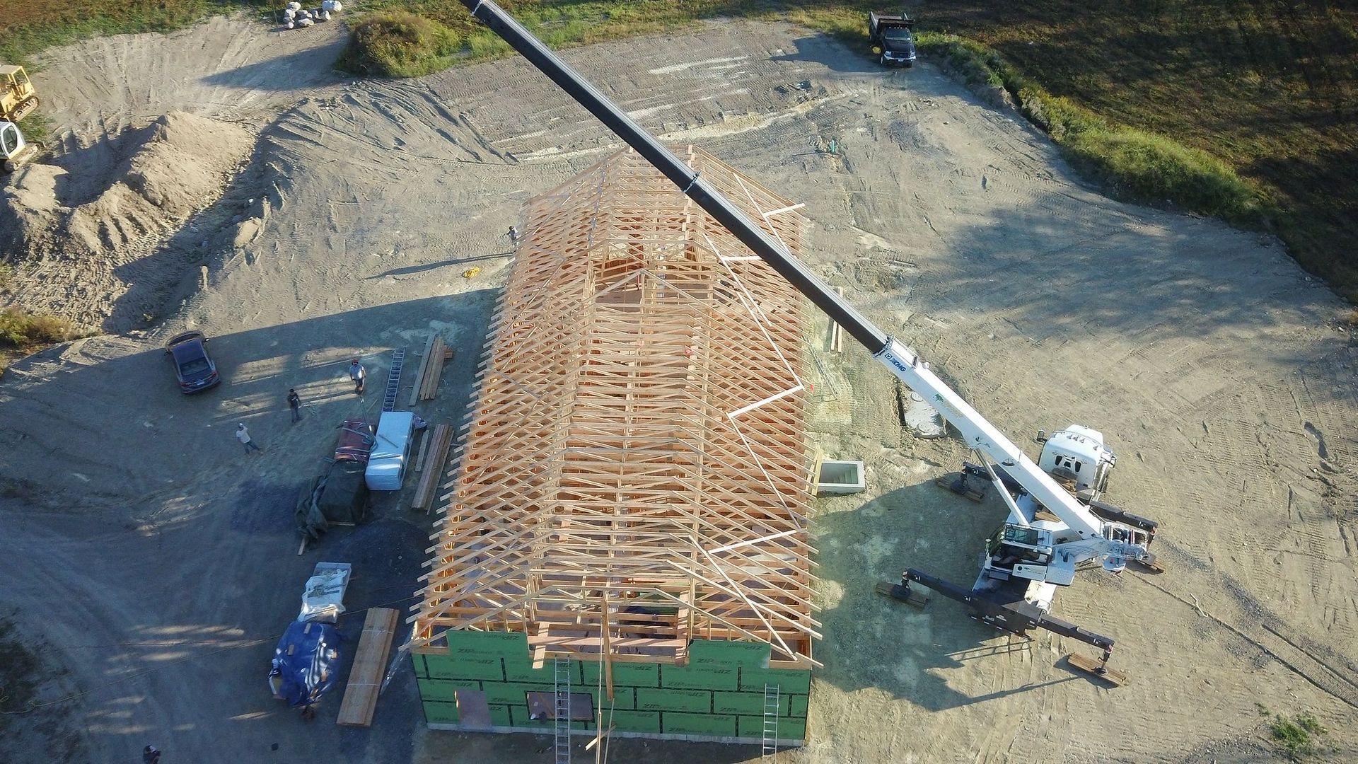 Construction site, crane lifting roof trusses onto a partially framed building; exterior shot.