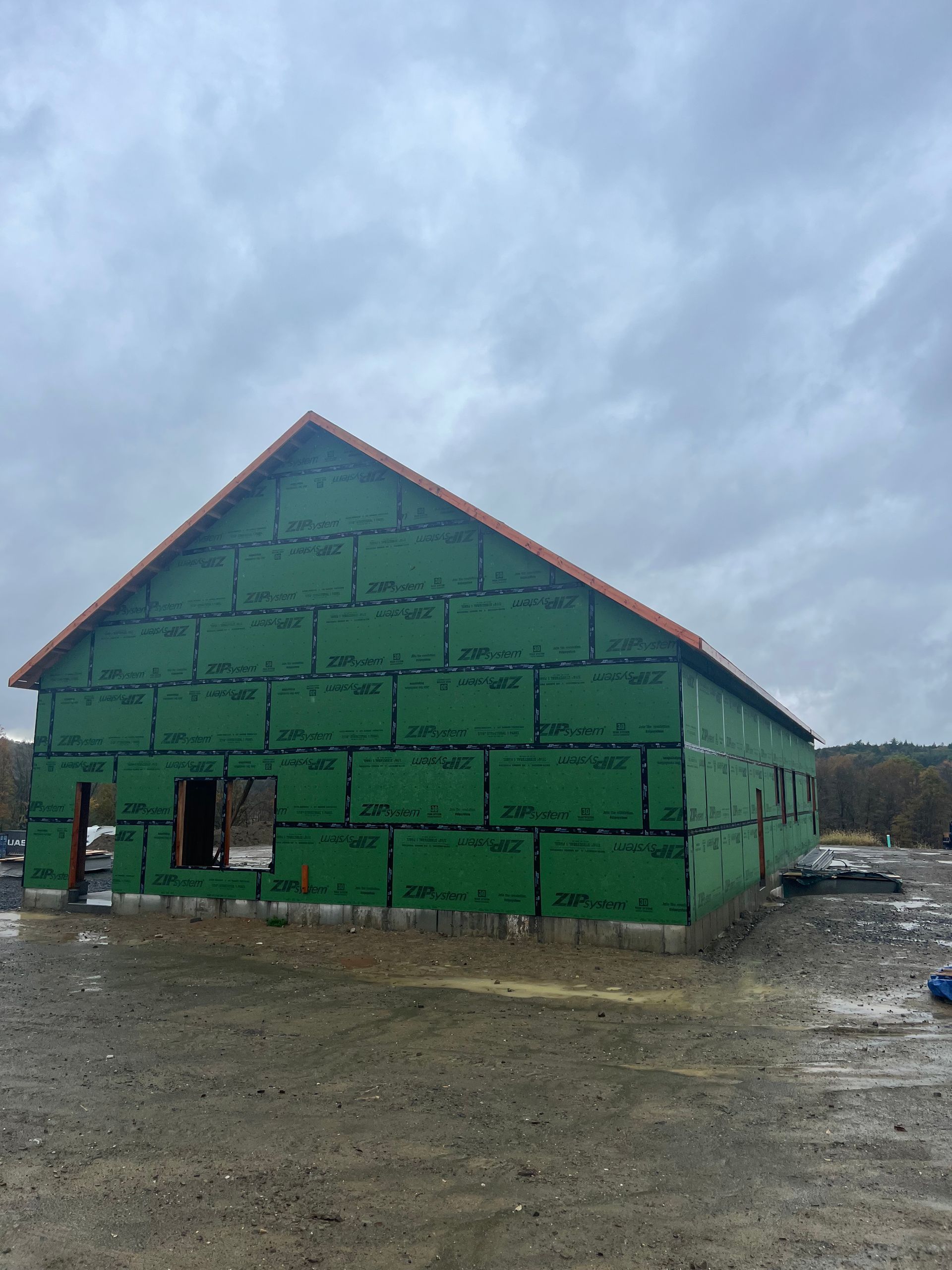 Building under construction, green sheathing, red roof tiles, cloudy sky.