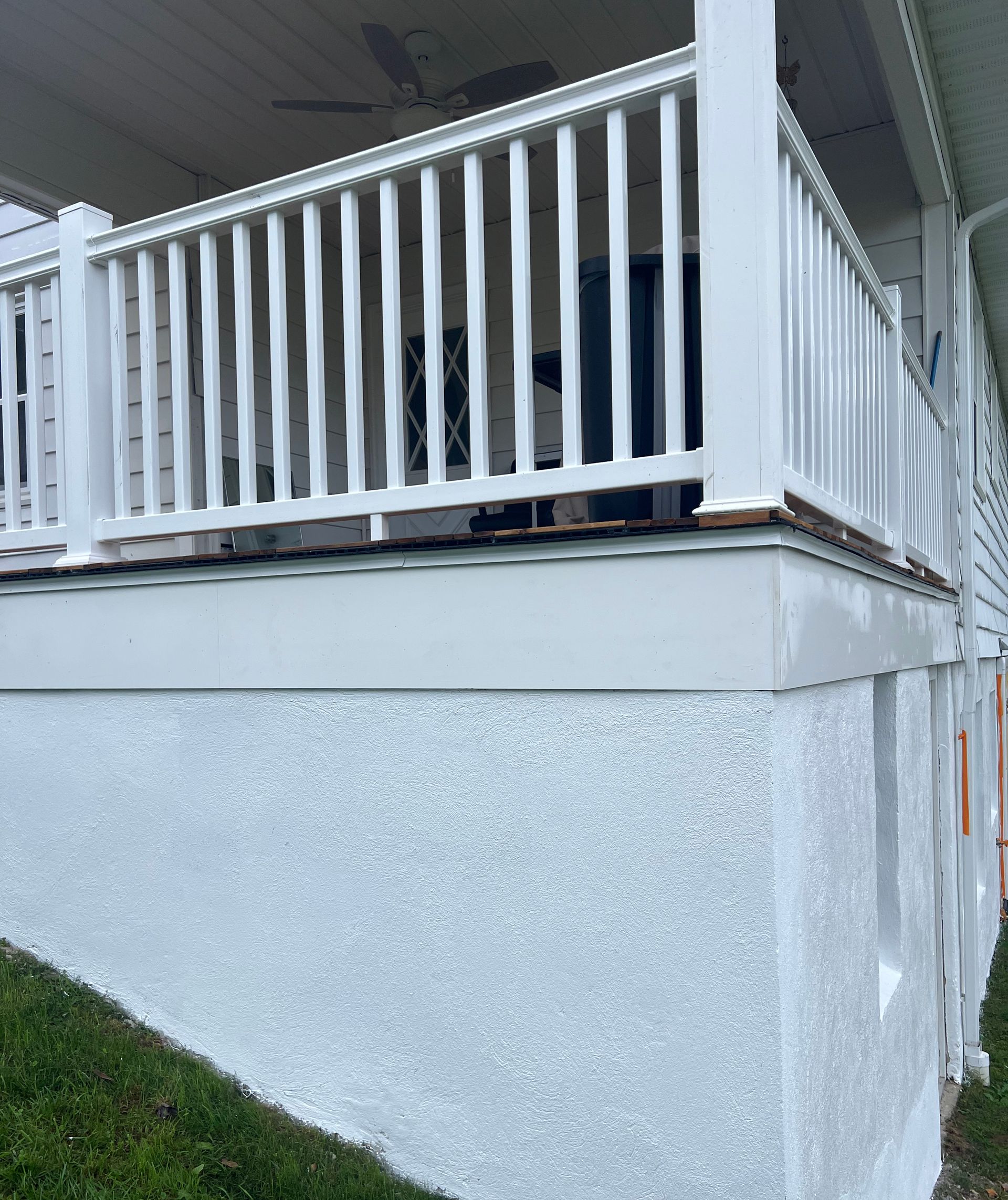 White porch with railing and stucco siding. Grass in the foreground.