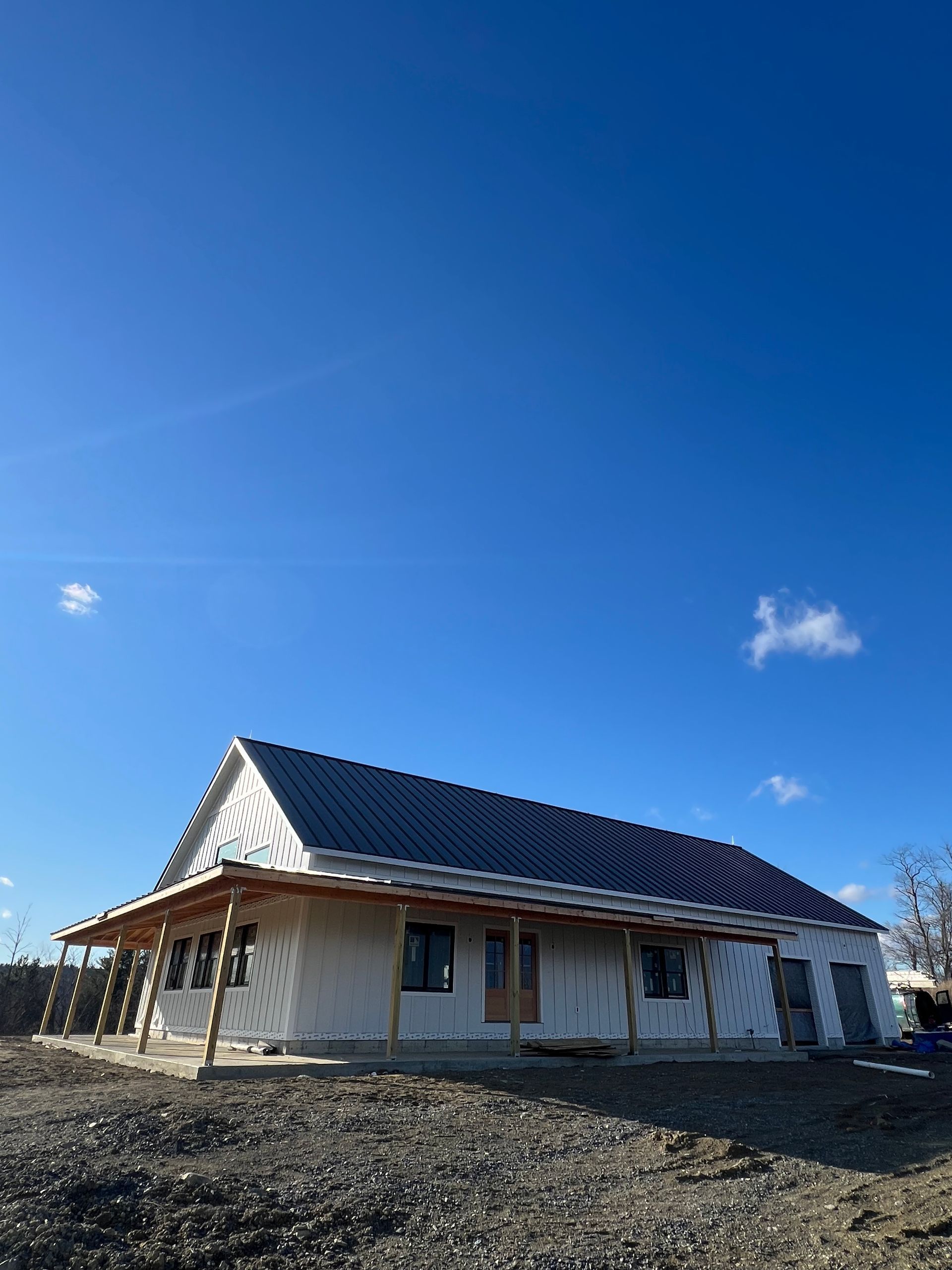 A white house under construction with a dark roof and wooden porch framing against a clear blue sky.