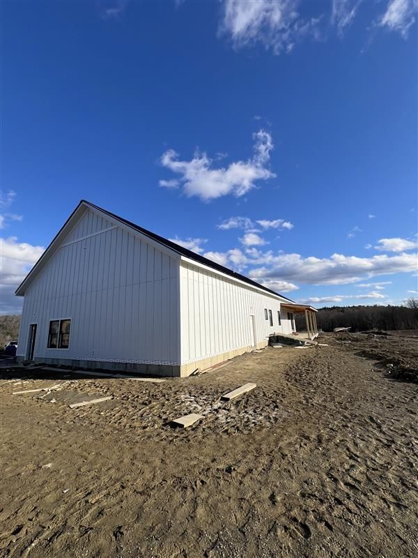 A newly constructed white pole barn with vertical siding sits on a dirt lot under a clear blue sky with light clouds.