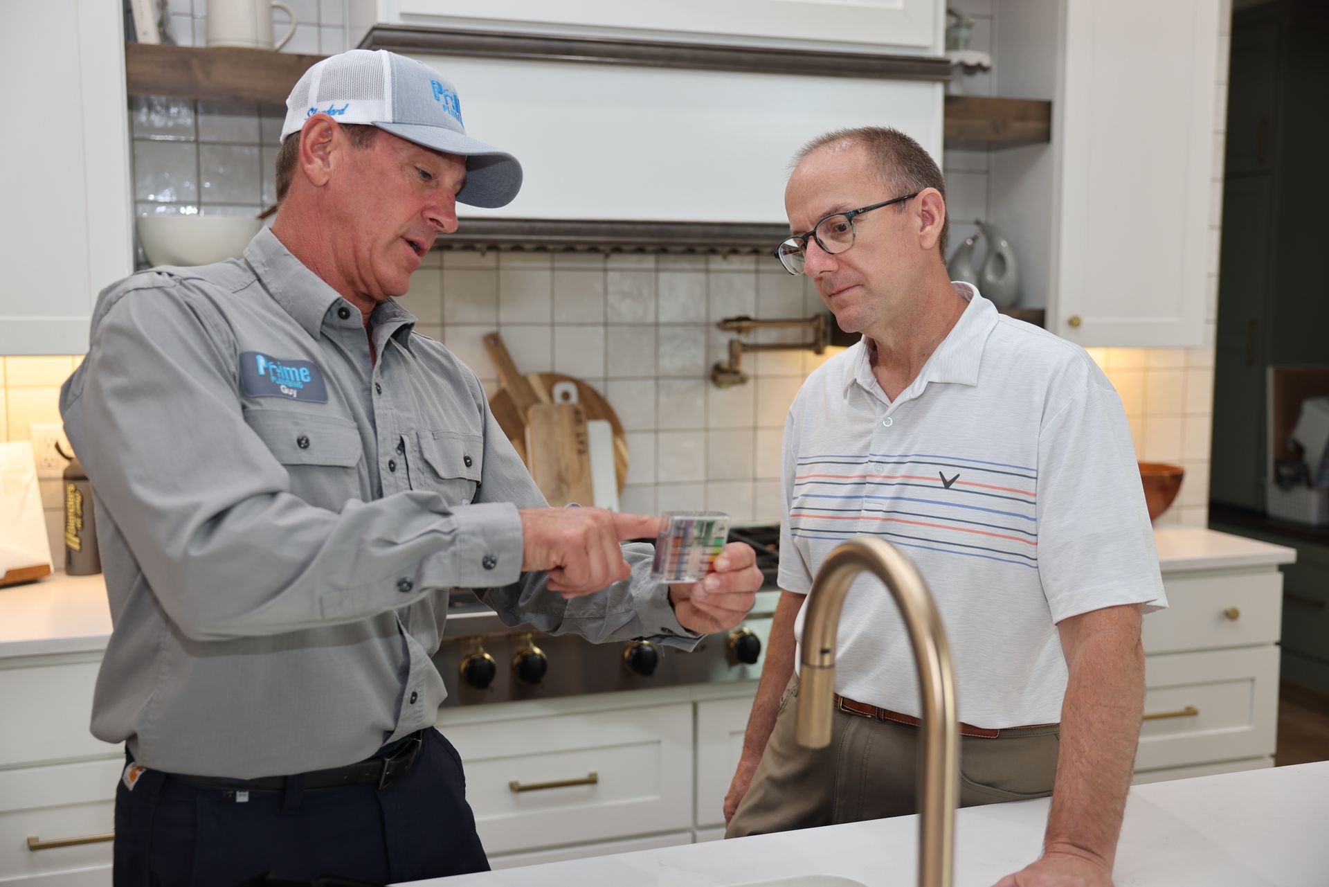 Plumber showing a client a metal part in a modern kitchen.