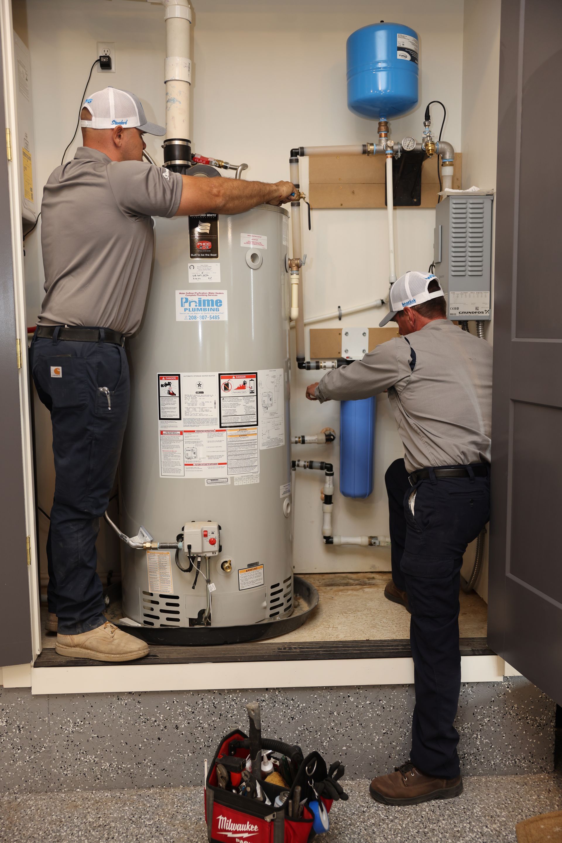 Two plumbers installing a water heater in an enclosed utility room.