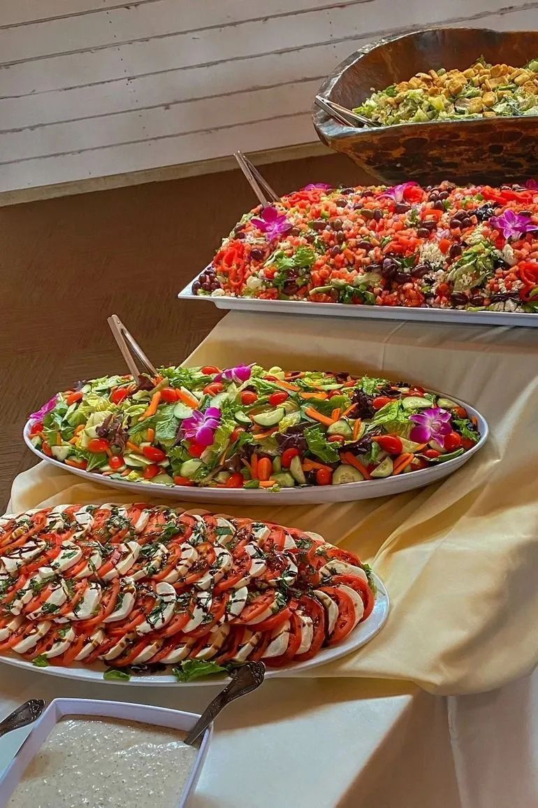 A buffet table with several platters of salad, including a caprese salad with tomato, mozzarella, and balsamic glaze.