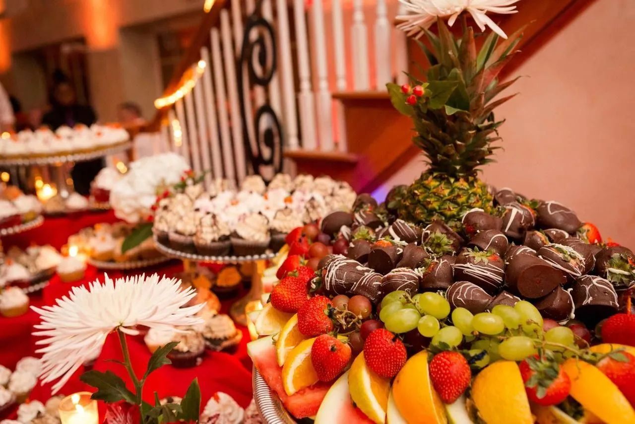 A vibrant fruit platter with chocolate-covered strawberries, grapes, and citrus, displayed at a formal event with cupcakes.