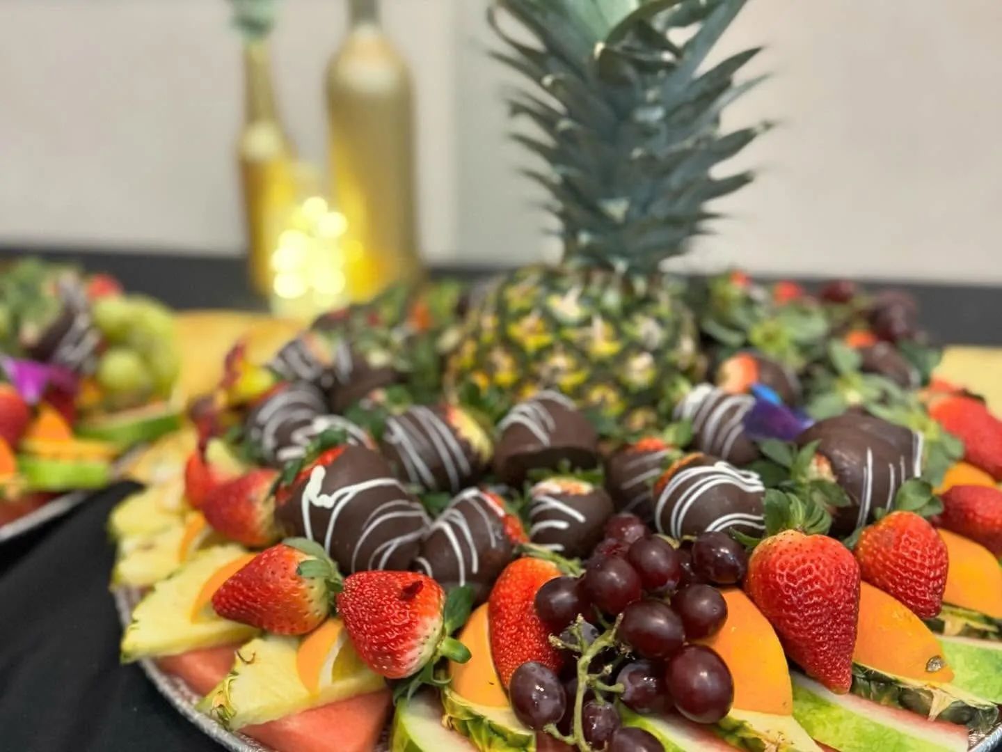 A fruit platter featuring chocolate-dipped strawberries, grapes, pineapple, and citrus slices, centered by a pineapple.