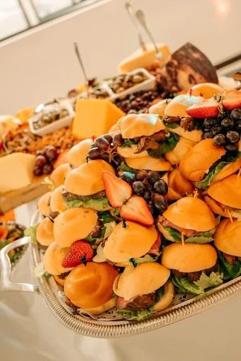 A silver platter stacked with mini sandwiches, decorated with grapes and sliced strawberries, at a catered event.