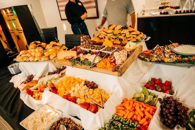 A buffet table overflowing with an assortment of appetizers, cheese, fruits, vegetables, and sliders.
