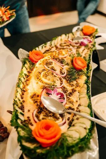 A large, oval platter of smoked salmon garnished with cucumber slices, capers, red onion rings, and carrot roses.