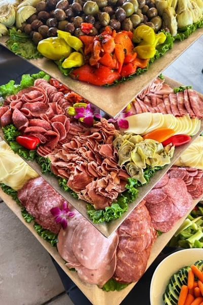 A multi-tiered platter featuring various deli meats, olives, roasted peppers, and artichoke hearts arranged on lettuce.