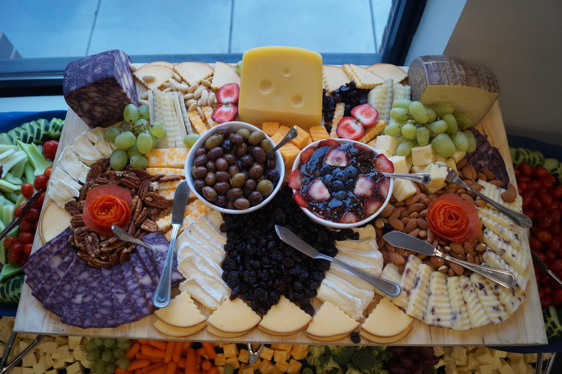 A large charcuterie board featuring various cheeses, meats, crackers, grapes, olives, nuts, and a berry compote.