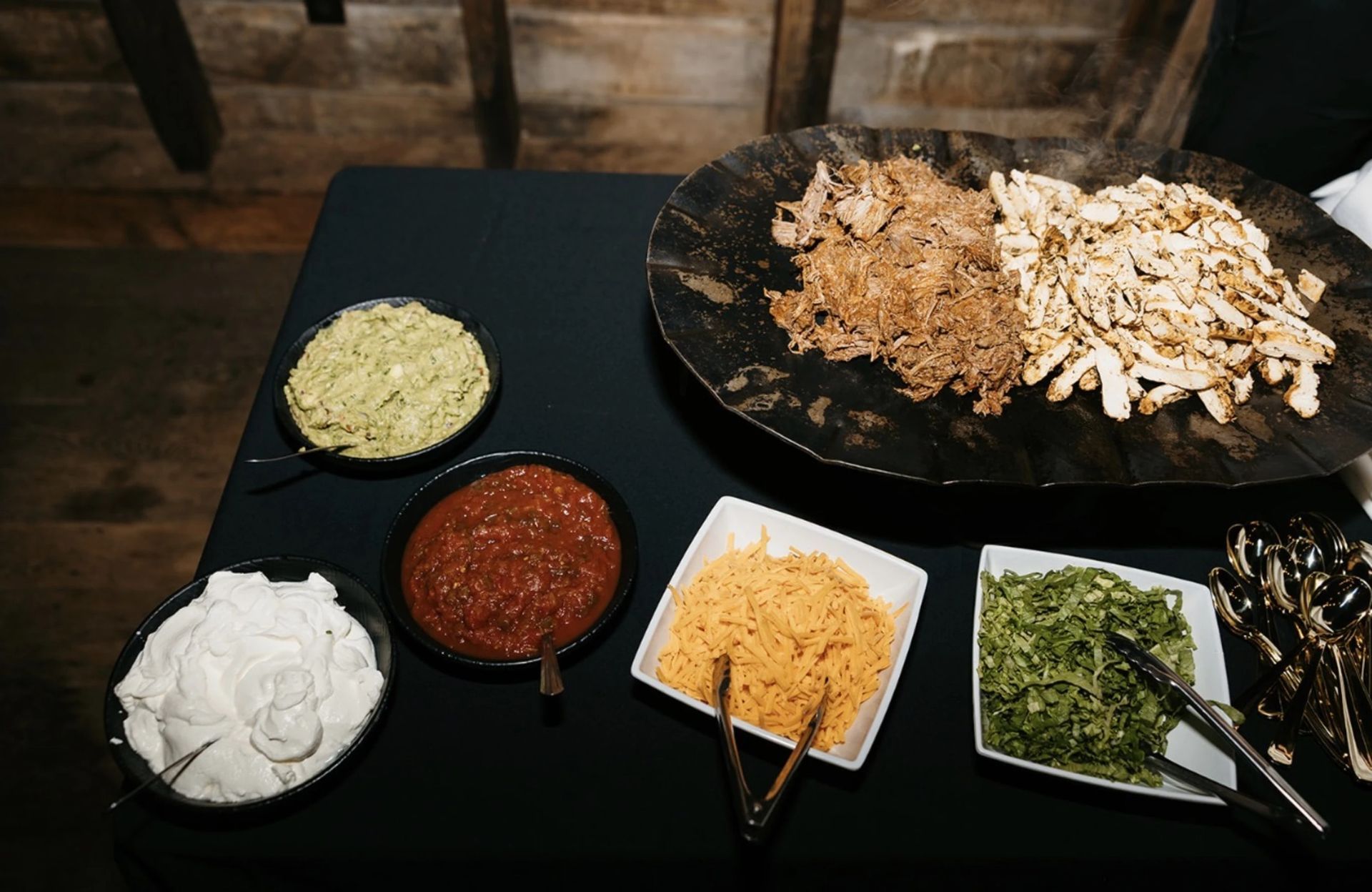 Buffet of assorted toppings in bowls beside a large plate of shredded vegetables on a dark table