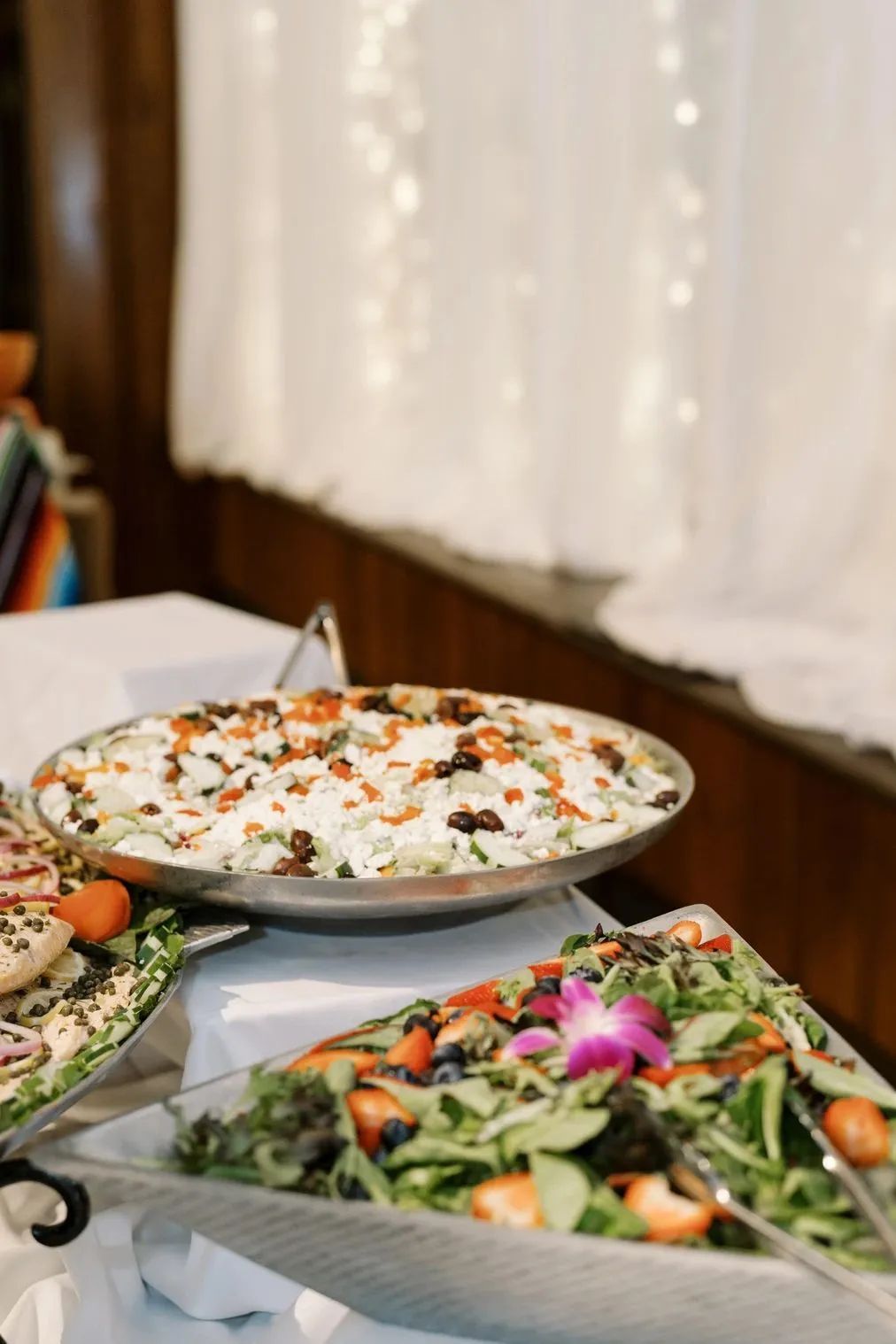 A buffet table displays two bowls of fresh salads, one with a creamy dressing and the other garnished with a purple flower.