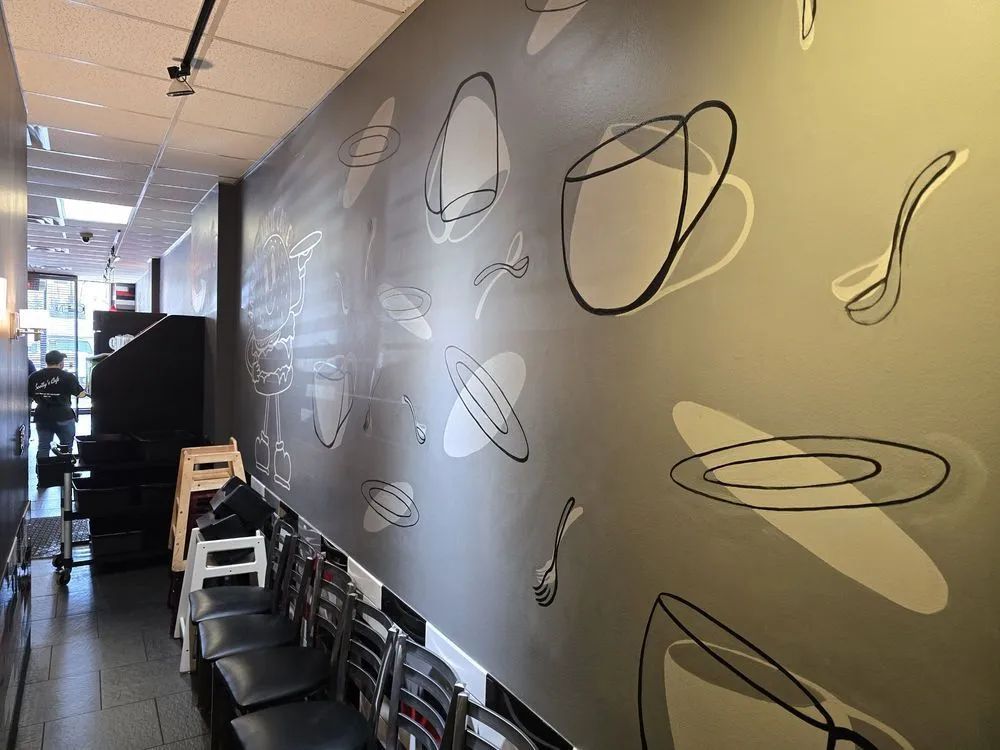 A grey interior wall features large, white and black minimalist line art of coffee cups, spoons, and plates.