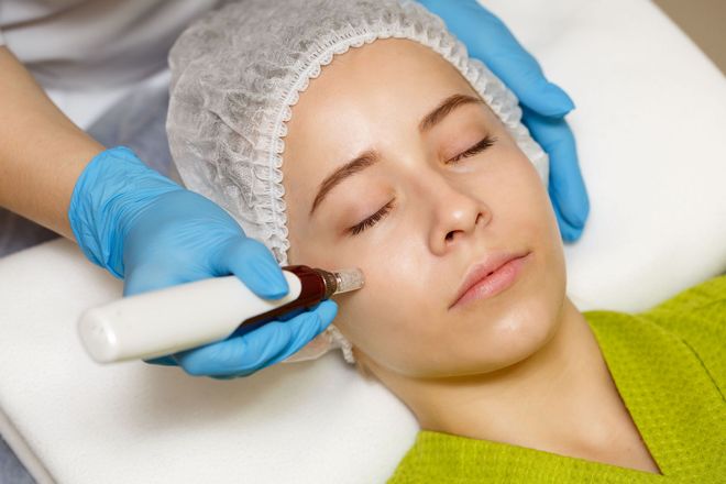 Cosmetic treatment with handheld device on woman’s cheek as she lies with eyes closed