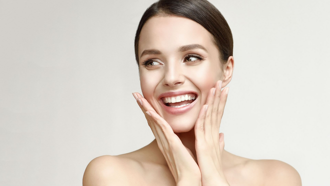 Smiling woman with hands on cheeks against a light background