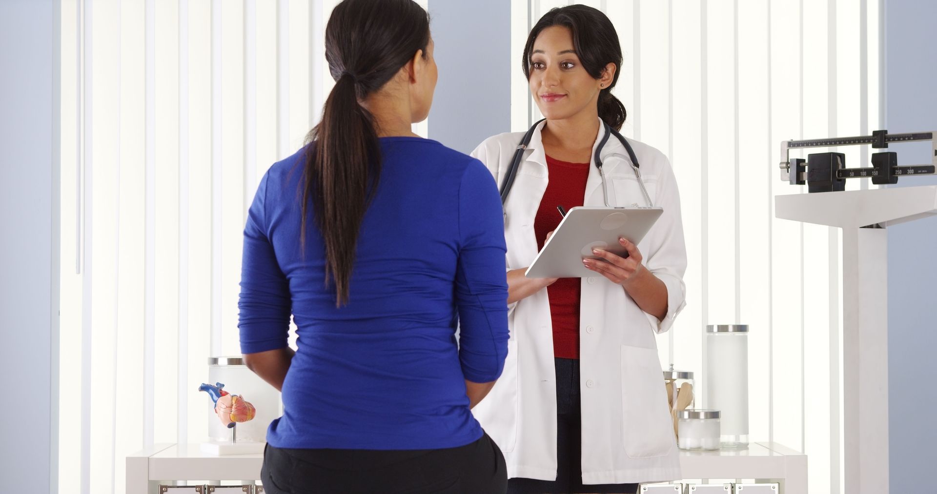 Doctor in white coat reviewing tablet with patient in blue shirt. Medical setting.